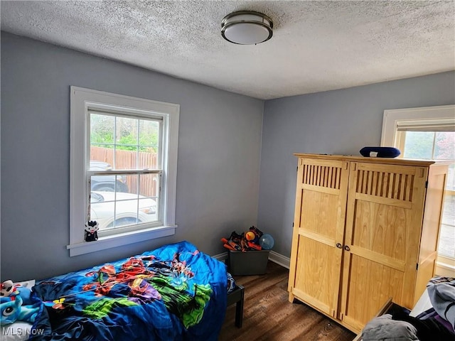 bedroom with dark wood-style floors, a textured ceiling, and multiple windows