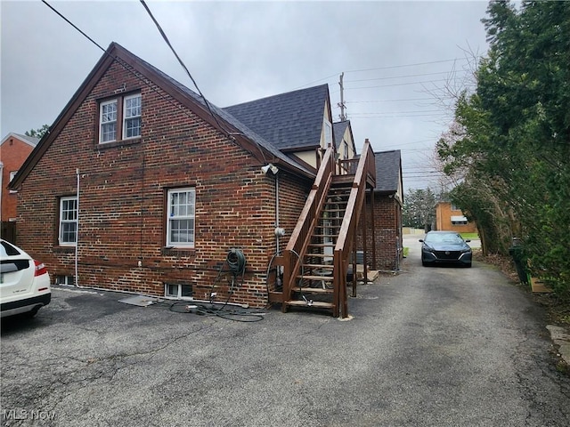 view of home's exterior with stairway, brick siding, and roof with shingles