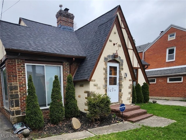tudor house featuring stucco siding, a chimney, a shingled roof, and brick siding