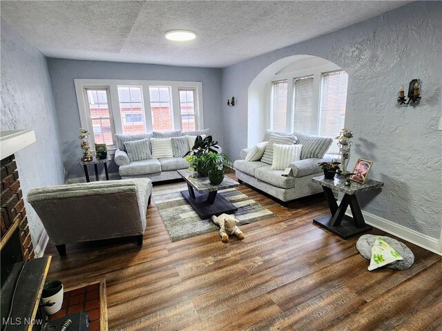 living room featuring a textured ceiling, a textured wall, arched walkways, a fireplace, and wood finished floors