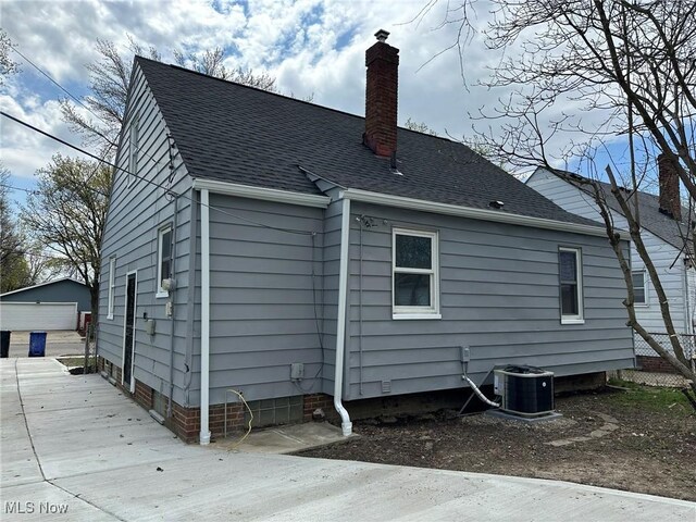 back of property featuring a chimney, a garage, a shingled roof, and central air condition unit