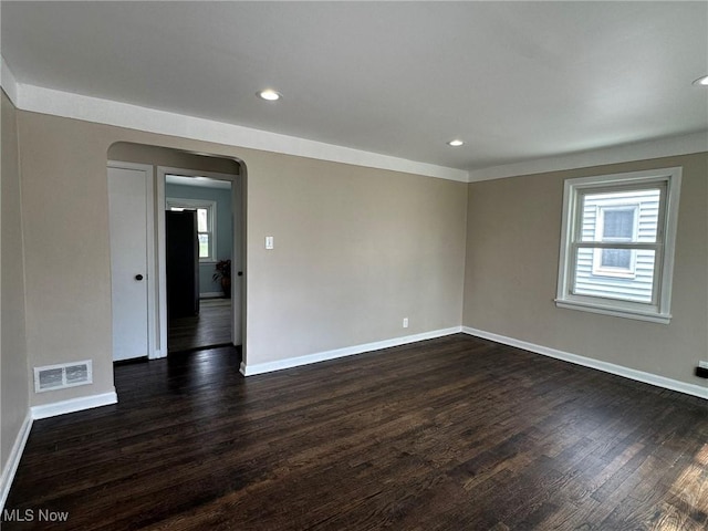 spare room with baseboards, visible vents, arched walkways, and plenty of natural light