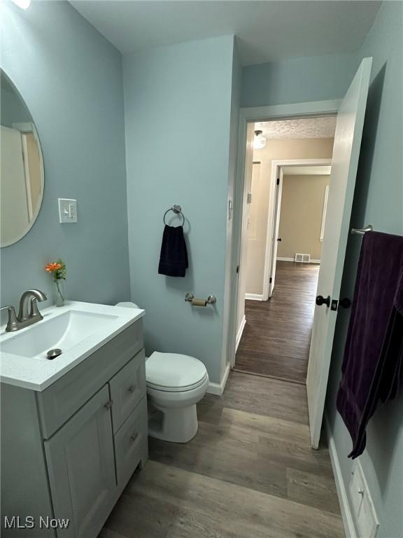 bathroom with toilet, vanity, wood finished floors, and baseboards