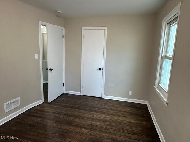 unfurnished bedroom with visible vents, multiple windows, and dark wood-type flooring