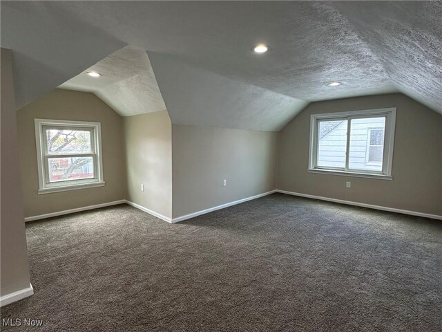 additional living space featuring recessed lighting, baseboards, dark carpet, a textured ceiling, and lofted ceiling