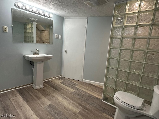 bathroom featuring wood finished floors, a walk in shower, toilet, baseboards, and visible vents