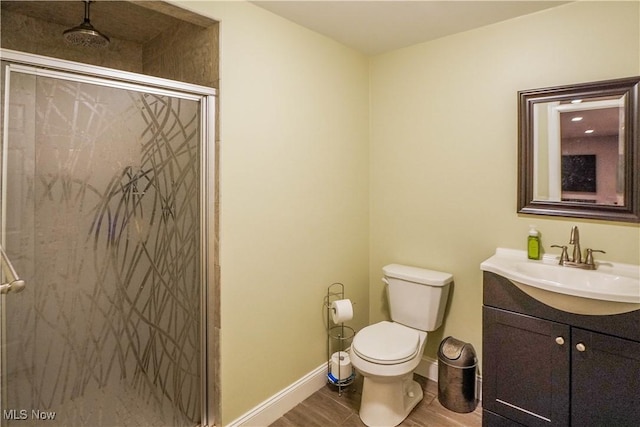 full bath featuring a shower stall, vanity, toilet, baseboards, and wood finished floors