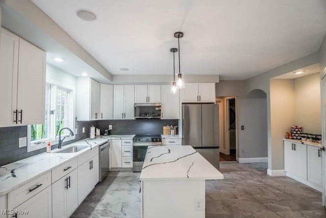 kitchen featuring decorative backsplash, a sink, appliances with stainless steel finishes, a kitchen island, and arched walkways