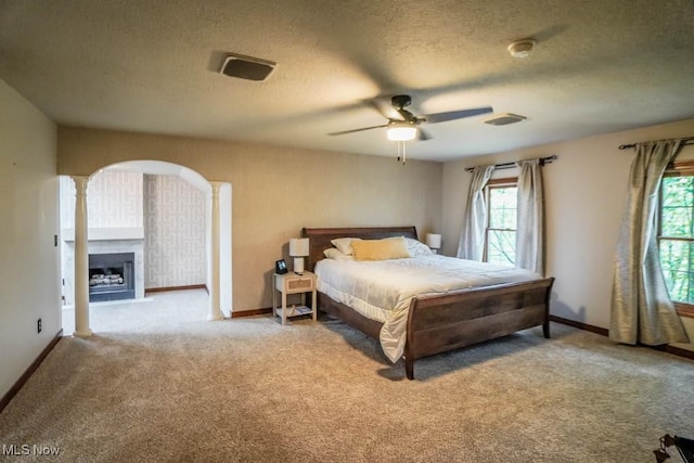 carpeted bedroom featuring a textured ceiling, baseboards, arched walkways, and multiple windows
