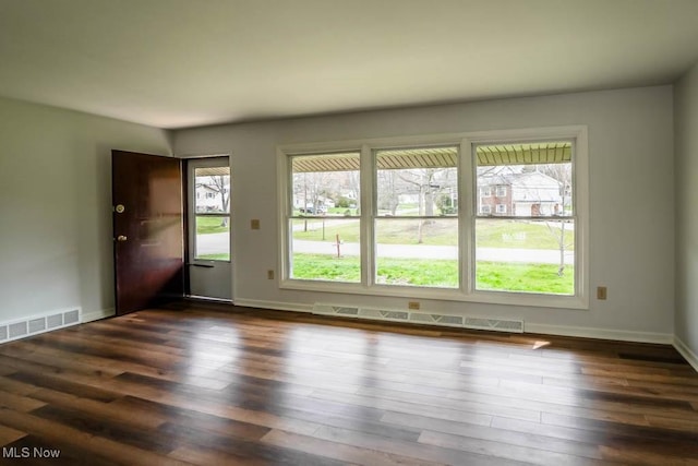 interior space with dark wood finished floors, visible vents, a baseboard heating unit, and plenty of natural light