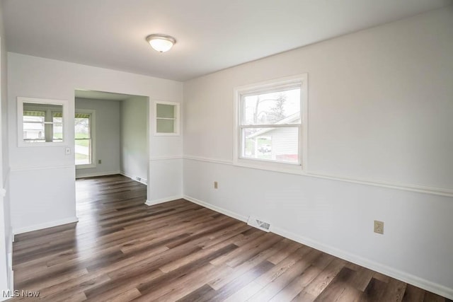 empty room featuring a wealth of natural light, dark wood-type flooring, and baseboards