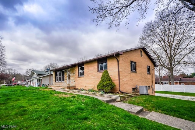 view of side of property featuring brick siding, central air condition unit, a yard, and fence