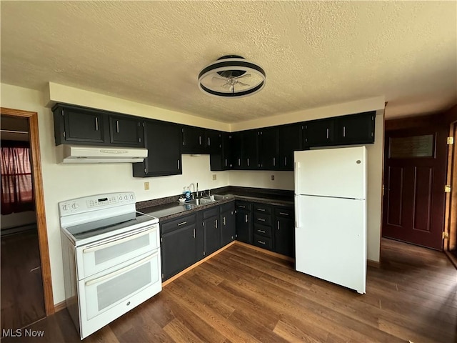 kitchen featuring white appliances, under cabinet range hood, dark countertops, dark cabinetry, and a sink