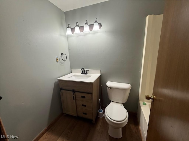 bathroom featuring baseboards, wood finished floors, toilet, and vanity