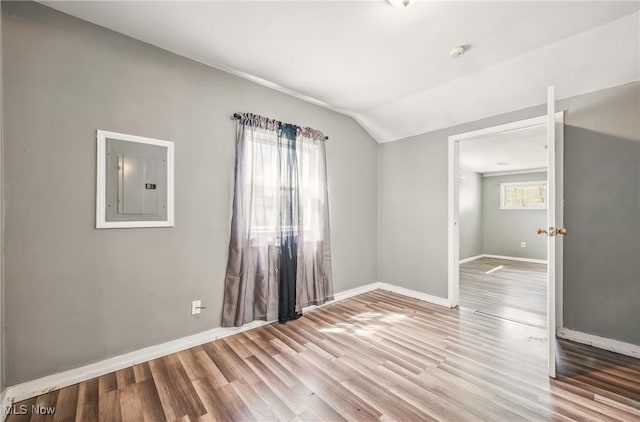 unfurnished room with lofted ceiling, wood finished floors, electric panel, and baseboards