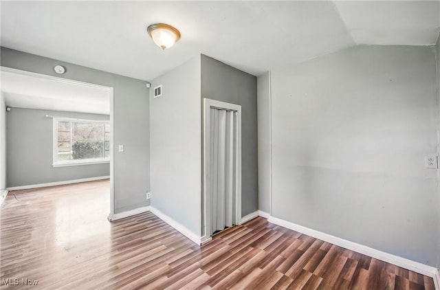 empty room featuring lofted ceiling, wood finished floors, visible vents, and baseboards