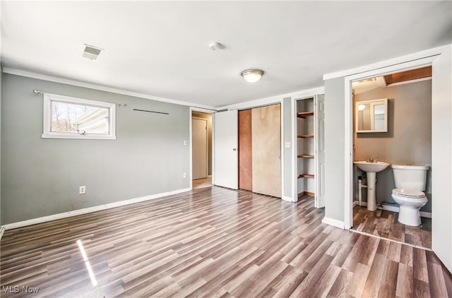 unfurnished bedroom with a sink, multiple closets, visible vents, baseboards, and wood finished floors