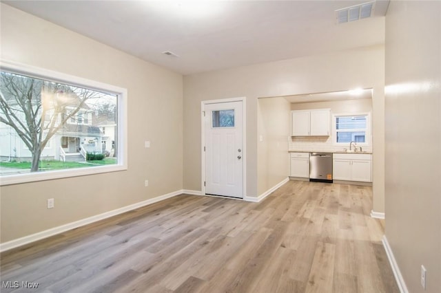 interior space featuring baseboards, visible vents, light wood-style flooring, and plenty of natural light
