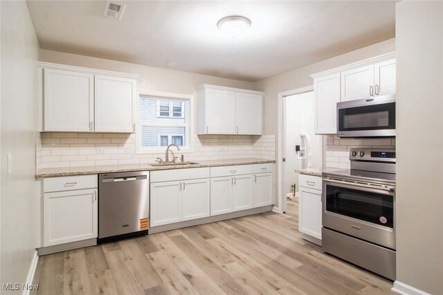 kitchen with a sink, stainless steel appliances, tasteful backsplash, light wood-style flooring, and white cabinetry