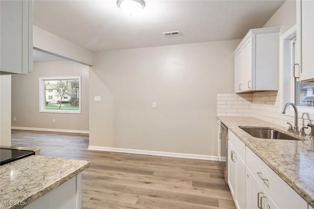 kitchen with a sink, light wood-type flooring, visible vents, light stone counters, and white cabinets