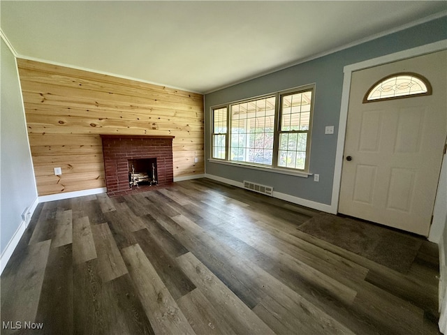 unfurnished living room featuring wood walls, visible vents, baseboards, dark wood finished floors, and a brick fireplace