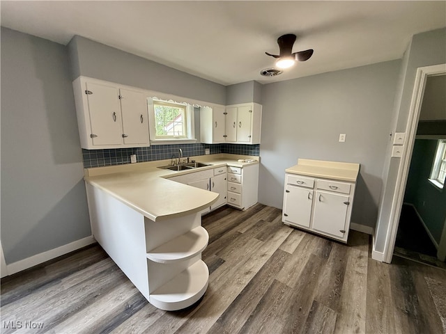 kitchen with light countertops, backsplash, a sink, white cabinetry, and dark wood-type flooring