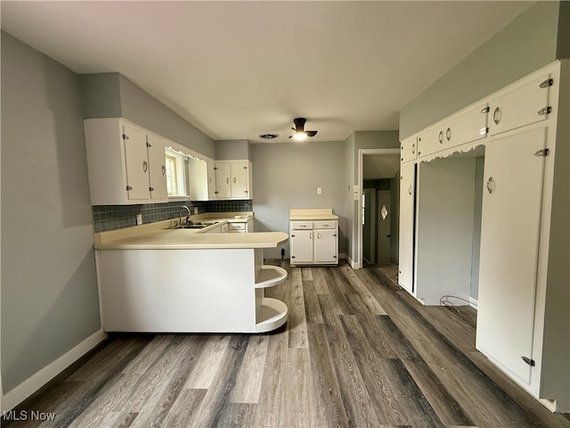 kitchen featuring decorative backsplash, white cabinets, a sink, dark wood-style floors, and a peninsula