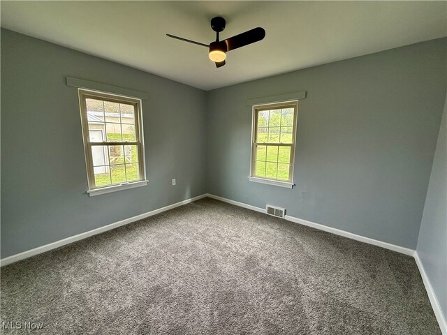 spare room with dark carpet, visible vents, a ceiling fan, and baseboards