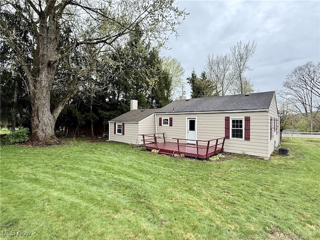 rear view of property with roof with shingles, a deck, a yard, and a chimney