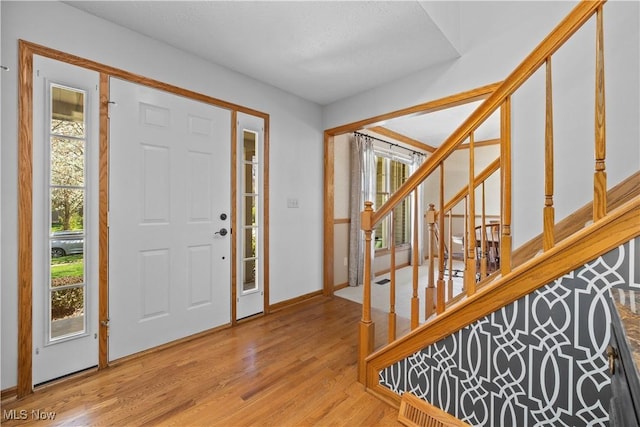 entryway featuring light wood-style floors, baseboards, and stairs