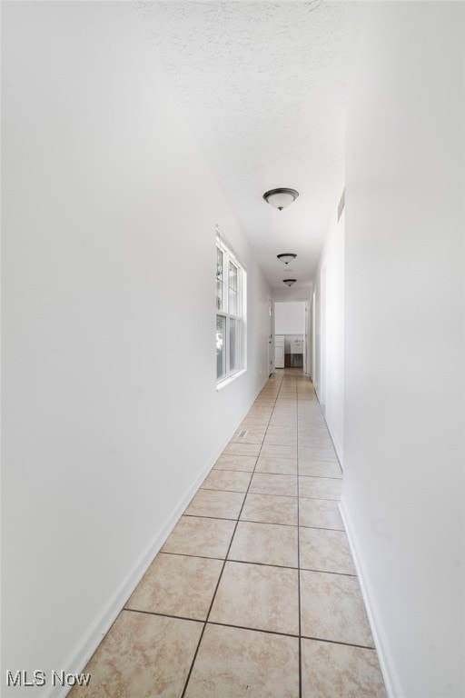hall with light tile patterned floors, a textured ceiling, visible vents, and baseboards