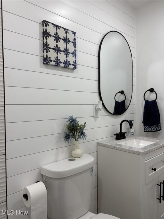 half bathroom with toilet, wood walls, and vanity