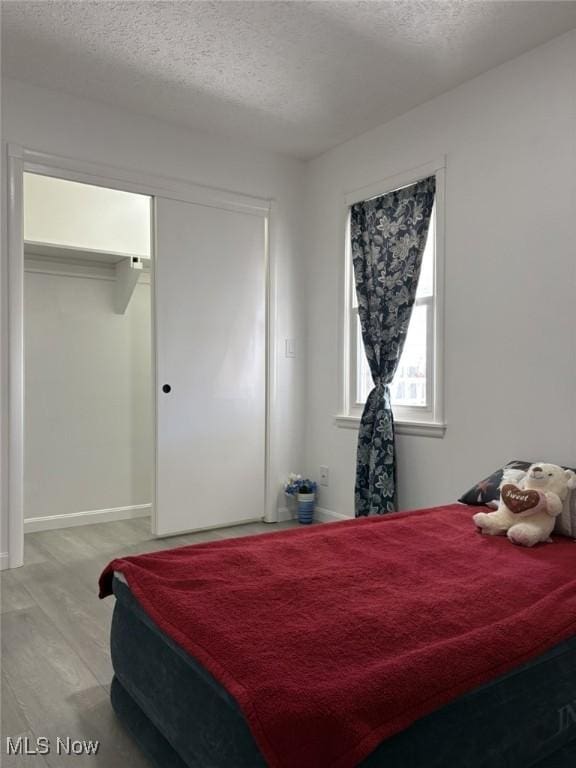 bedroom with baseboards, a closet, light wood-type flooring, and a textured ceiling