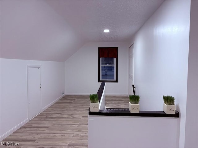 corridor with a textured ceiling, wood finished floors, baseboards, lofted ceiling, and recessed lighting