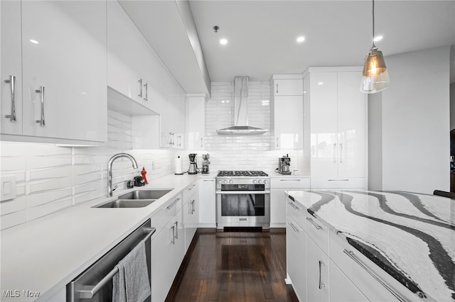 kitchen with wall chimney range hood, white cabinetry, decorative backsplash, a sink, and appliances with stainless steel finishes