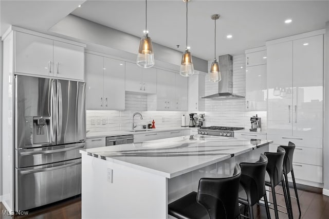 kitchen featuring a sink, a kitchen island, wall chimney range hood, white cabinets, and appliances with stainless steel finishes