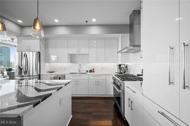 kitchen with stainless steel appliances, decorative light fixtures, wall chimney range hood, white cabinets, and a sink