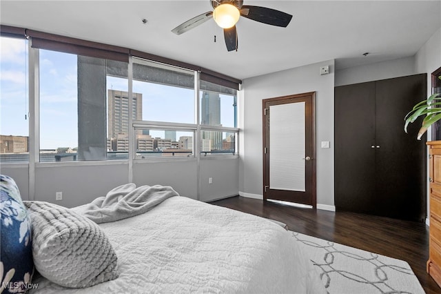 bedroom featuring a view of city, wood finished floors, a ceiling fan, and baseboards