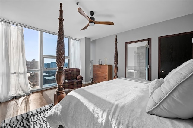 bedroom featuring a view of city, wood finished floors, ensuite bathroom, and a ceiling fan