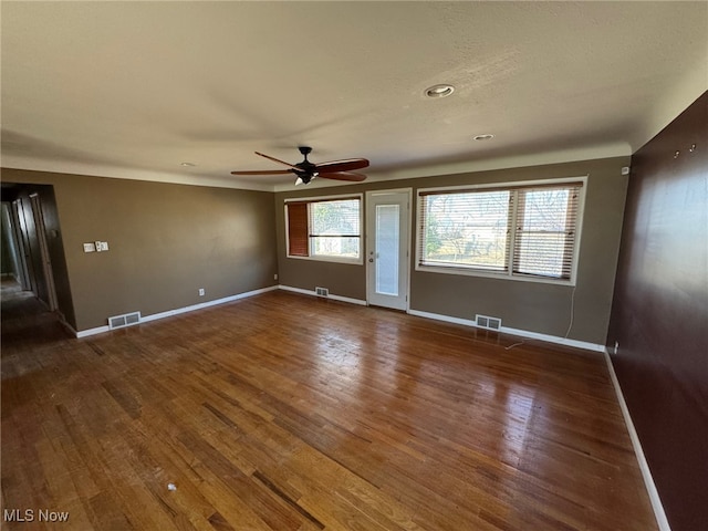 unfurnished room with dark wood-style flooring, visible vents, ceiling fan, and baseboards