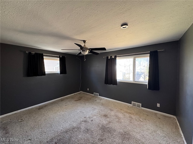 carpeted spare room featuring a textured ceiling, visible vents, and a ceiling fan