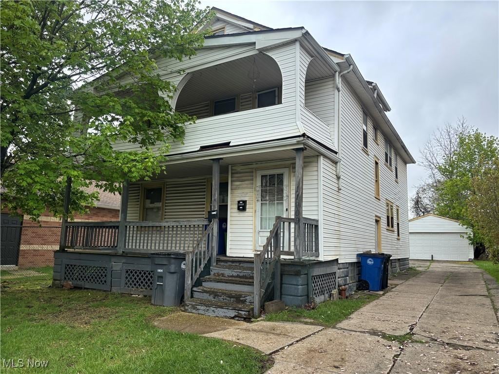 view of front facade featuring a porch, an outdoor structure, a detached garage, and a balcony