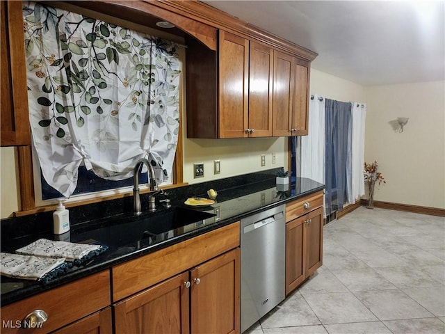 kitchen featuring dark stone counters, a sink, light tile patterned flooring, dishwasher, and brown cabinetry