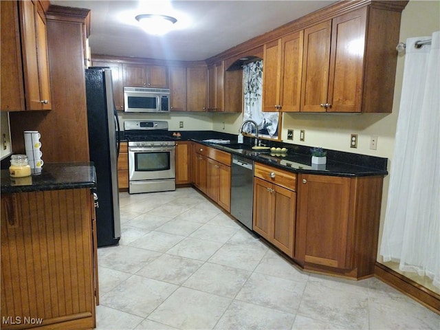 kitchen featuring dark stone countertops, a sink, appliances with stainless steel finishes, and brown cabinetry