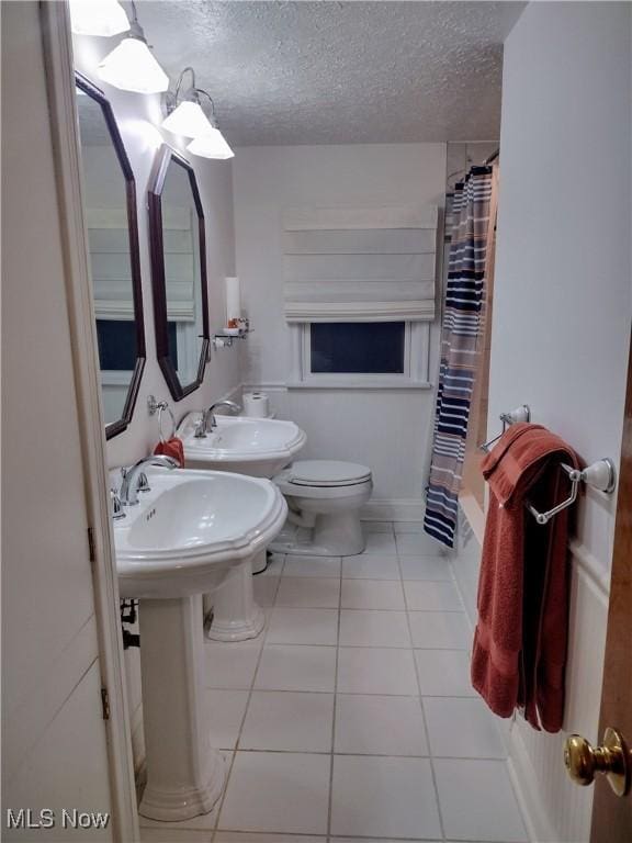 bathroom with tile patterned floors, a textured ceiling, toilet, and a sink