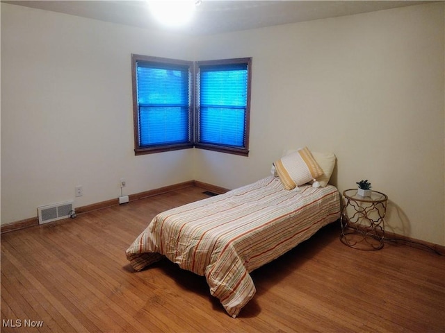 bedroom with baseboards, visible vents, and wood finished floors