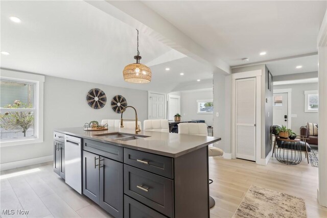kitchen featuring pendant lighting, light wood-style flooring, a sink, white dishwasher, and a kitchen island with sink