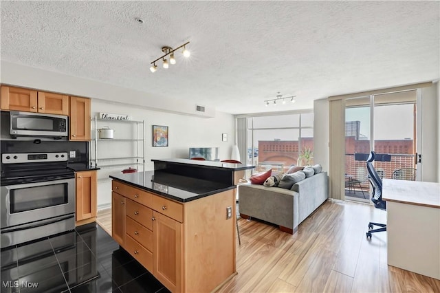 kitchen featuring stainless steel appliances, rail lighting, dark countertops, a textured ceiling, and wood finished floors