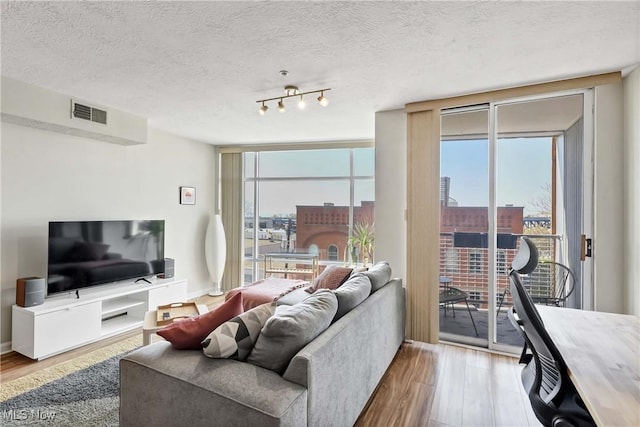 living area featuring visible vents, wood finished floors, a wall of windows, and a textured ceiling