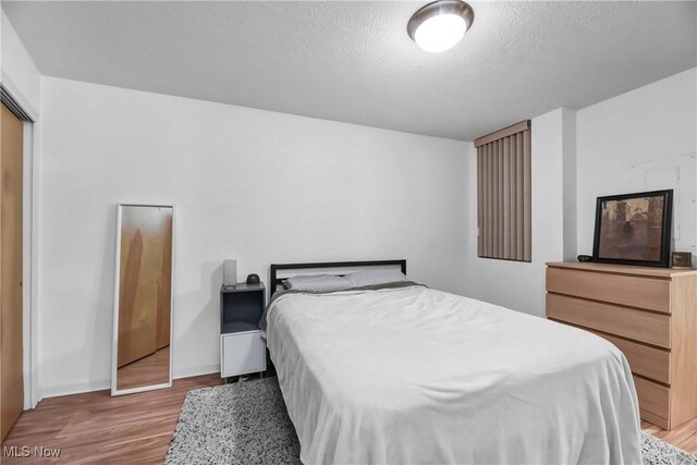 bedroom with a textured ceiling, light wood-style flooring, and baseboards